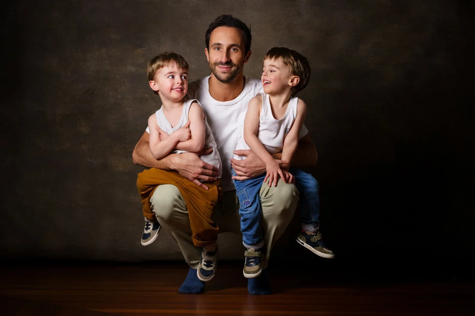 Un père assis avec ses deux garçons sur un fond brun au studio