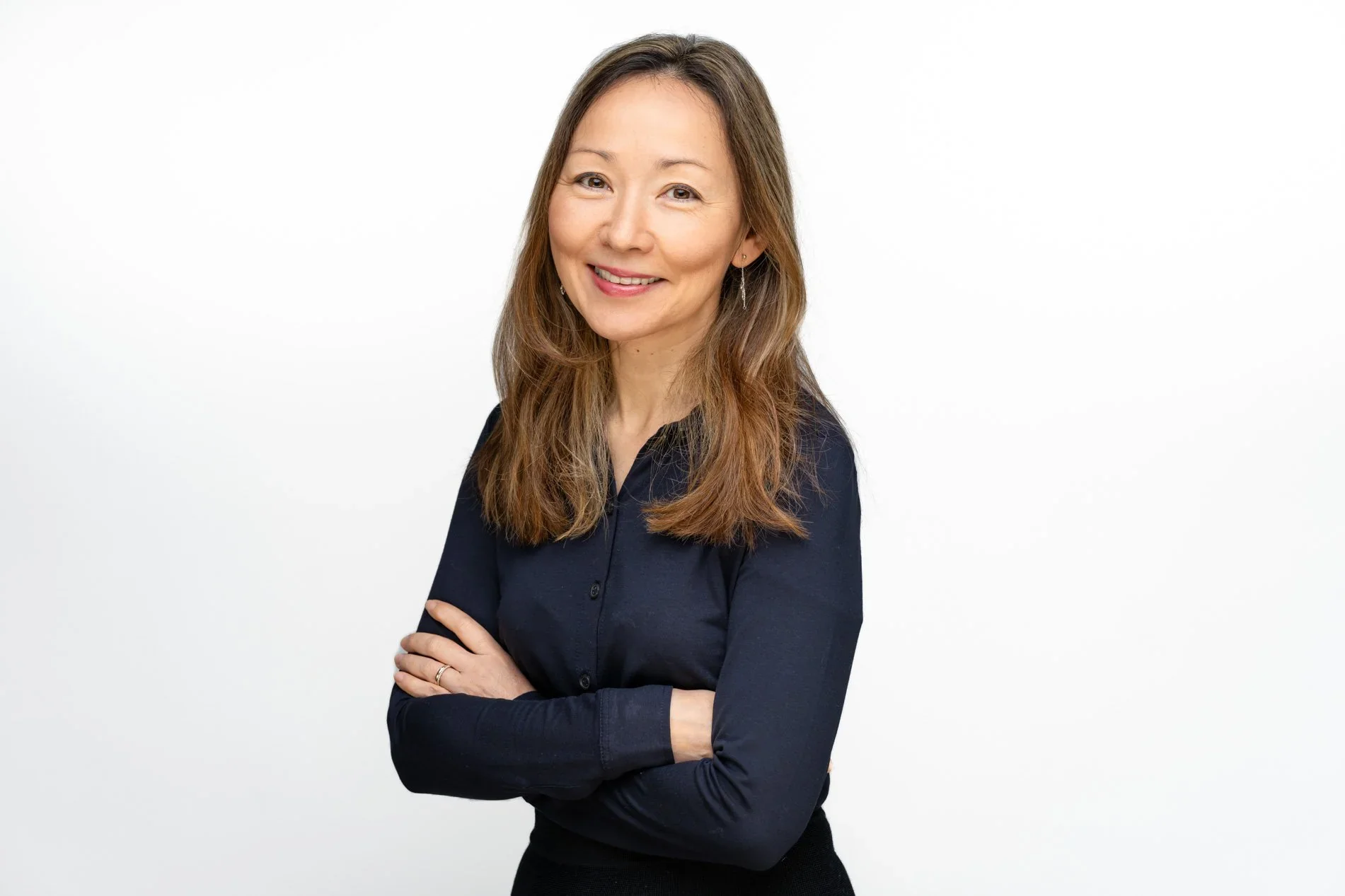 Femme souriante aux cheveux longs, bras croisés, en chemisier bleu foncé sur fond blanc