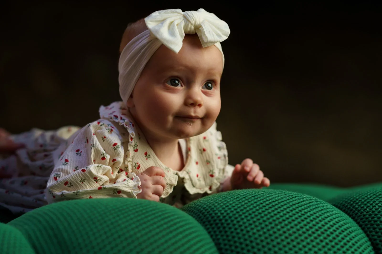 Bébé en tenue fleurie et bandeau à nœud blanc, en appui sur un tissu vert