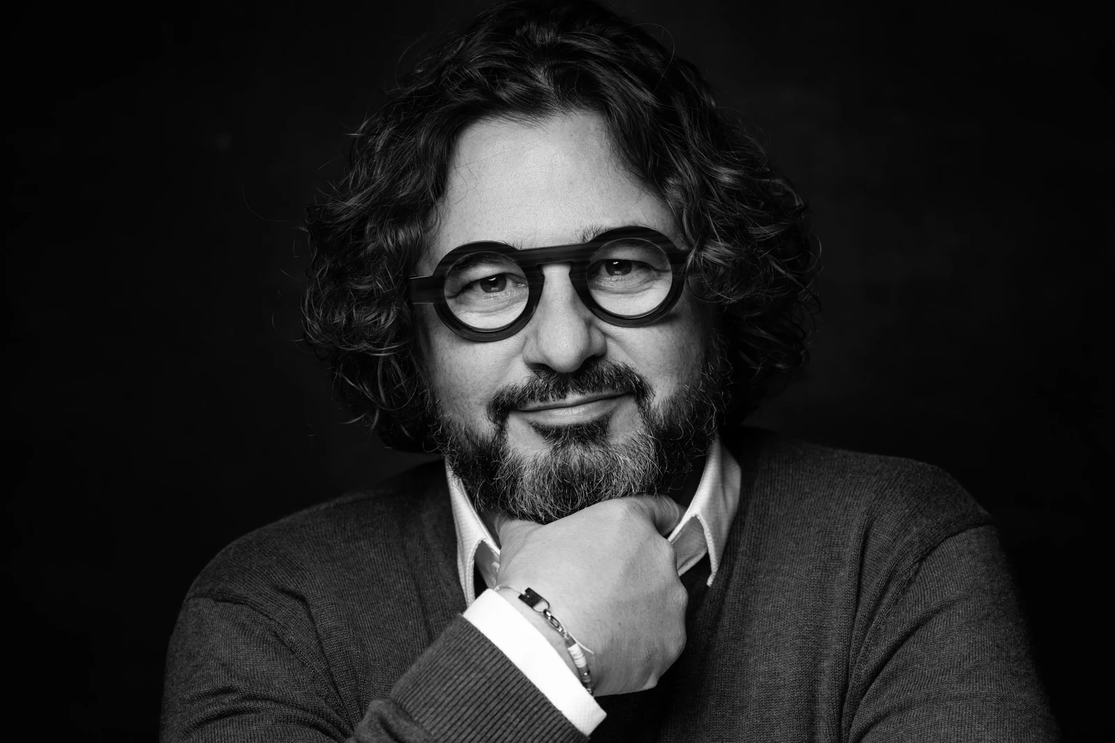 Portrait en noir et blanc d’un homme barbu à lunettes rondes, le menton appuyé sur sa main