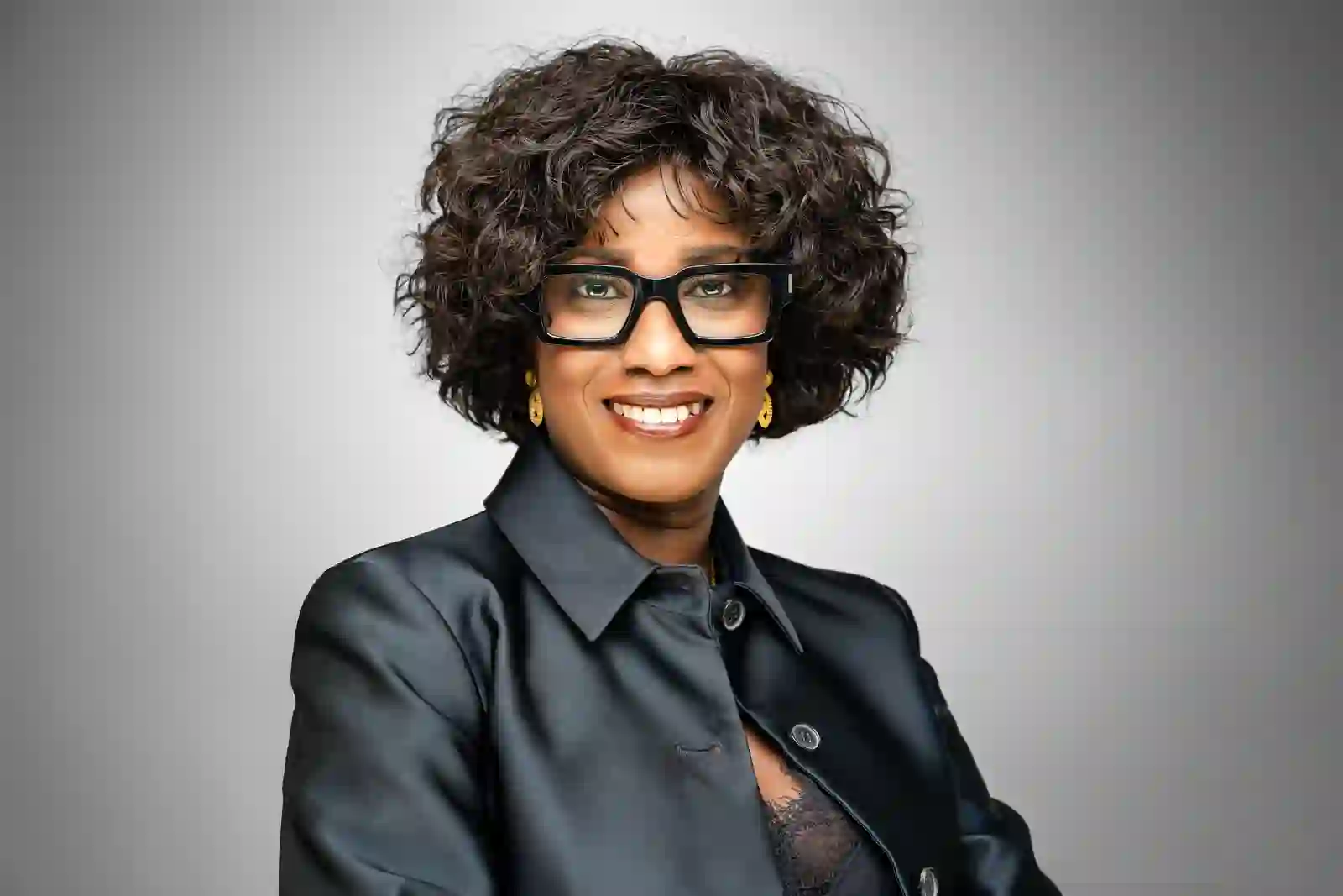 Femme souriante aux cheveux bouclés et grandes lunettes noires, en veste sombre brillante